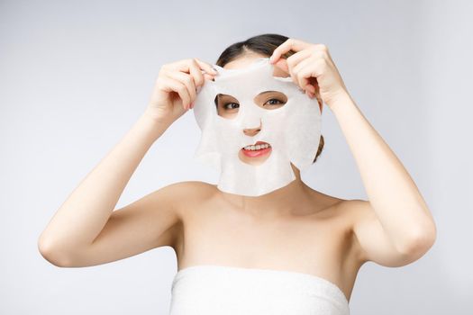 Beautiful asian woman applying paper sheet mask on her face white background.