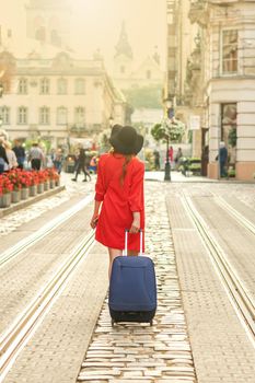 Beautiful young woman walking with a rolling suitcase on the tram track road in the old European city.