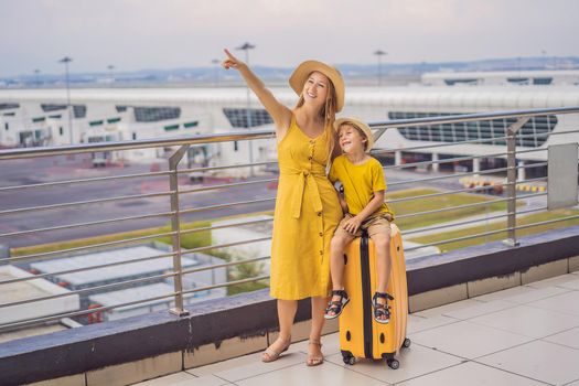 Family at airport before flight. Mother and son waiting to board at departure gate of modern international terminal. Traveling and flying with children. Mom with kid boarding airplane. yellow family look.