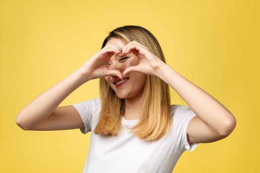 Young Asian woman show heart hand sign isolated on yellow background