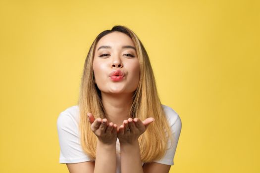 Beautiful young Asian woman blow a kiss isolated on yellow background.