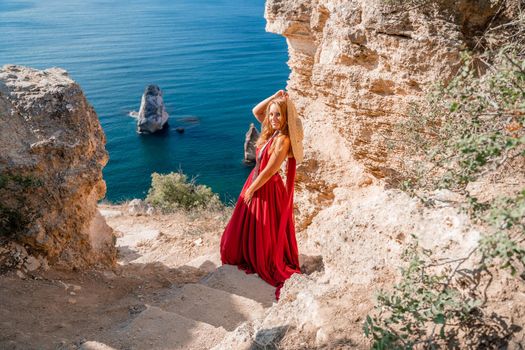 A woman in a flying red dress fluttering in the wind and a straw hat against the backdrop of the sea