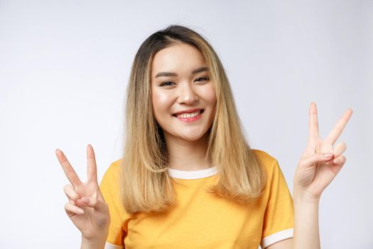 Happy young asian woman showing two fingers or victory gesture with blank copyspace area for text,Portrait of beautiful Asian woman isolated on white background.