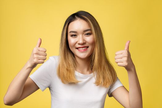 Young Asian woman show thumbs up on yellow background.
