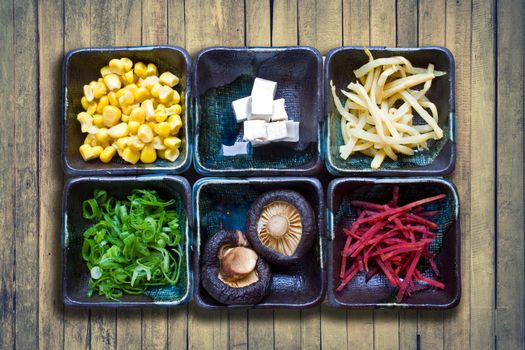 Ramen topping ingredients on a wooden background with sweet corn, tofu, shiitake, spring onion, soy sprouts