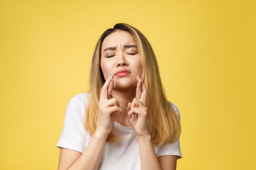 Young happy asian woman with fingers crossed on yellow background.