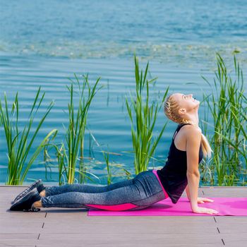 Healthy woman is stretching on the grass at the shore of the lake.