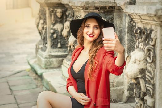 Happy young travel woman is taking selfie on the street of old European city.
