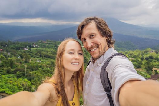 Man and woman making selfie on background of Batur volcano and Agung mountain view at morning from Kintamani, Bali, Indonesia.