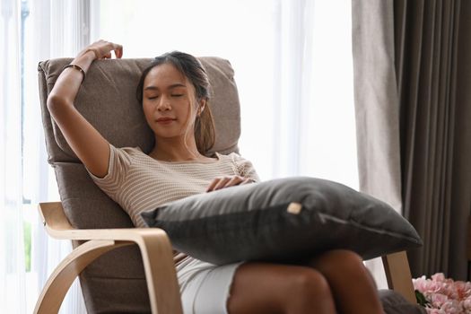 Relaxed young woman in casual clothes resting on comfortable armchair at home.