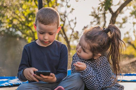 children look at the phone while sitting on a trampoline