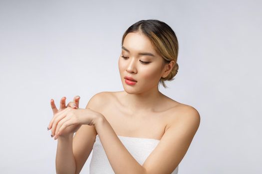 Asian woman applying cosmetic cream on skin on isolated white background.