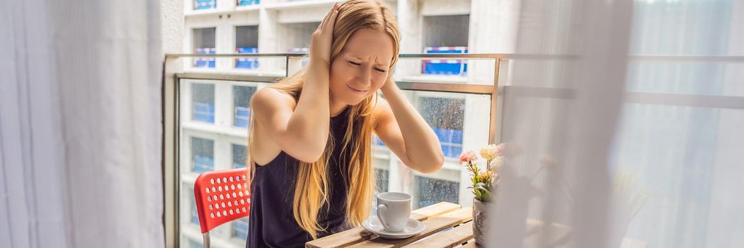 Young woman on the balcony annoyed by the building works outside. Noise concept. Air pollution from building dust. BANNER, LONG FORMAT