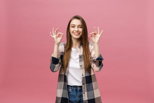 Attractive young adult woman showing ok sign. Expression emotion and feelings concept. Studio shot, isolated on pink background