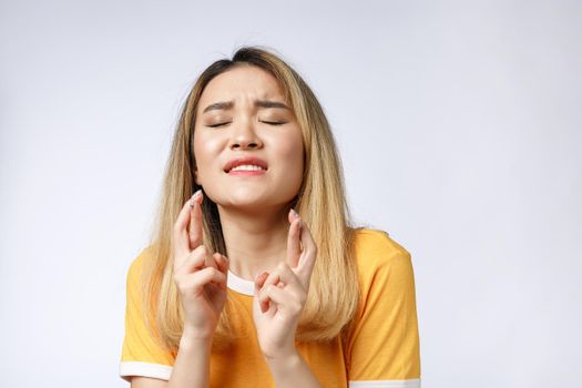 Portrait of praying young woman wearing casual clothing begging god please looking up with keeping fingers crossed isolated over gray background