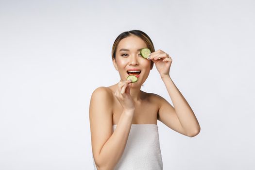 Young asian woman holding and eating cucumber slice in her hands isolated on white background.