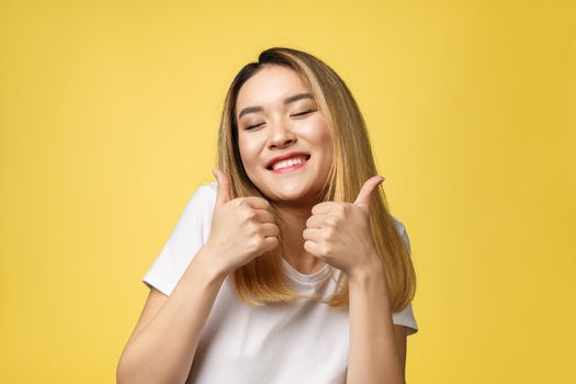 Young Asian woman show thumbs up on yellow background.