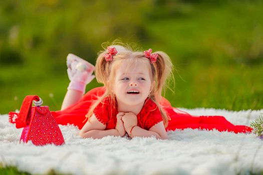 a girl in a red dress lies on a white blanket that is laid on the lawn