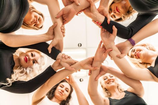 Team of people holding hands. Group of happy young women holding hands. Bottom view, low angle shot of human hands. Friendship and unity concept.