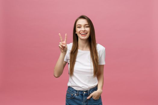 Portrait of a cheerful trendy woman showing two fingers sign over pink background.