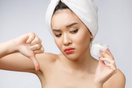 Beauty portrait of half-naked asian woman looking on camera and holding face cream on her palm isolated over white background copy space