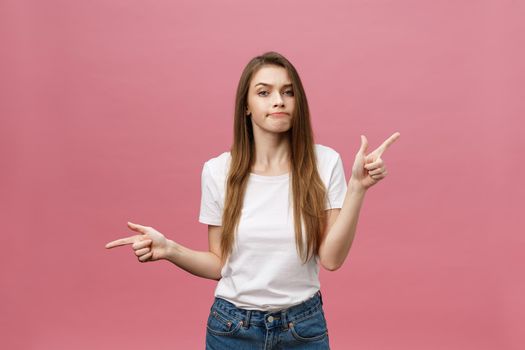 Closeup of serious strict young woman wears white shirt looks stressed and pointing up with finger isolated over pink background.