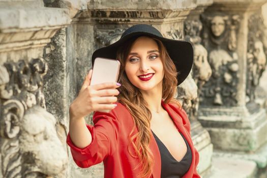 Happy young lady is taking photo of herself by smartphone on the city street.