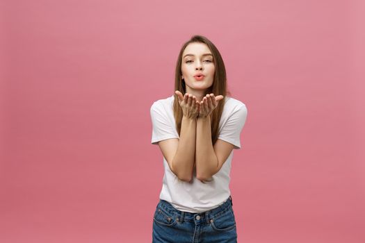 Beautiful woman with makeup and long blonde hair blows kiss, demonstrates her good feelings, says goodbye on distance, isolated over pink background.