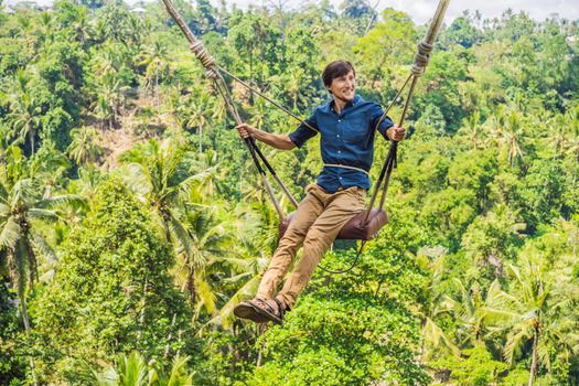 Young man swinging in the jungle rainforest of Bali island, Indonesia. Swing in the tropics. Swings - trend of Bali.
