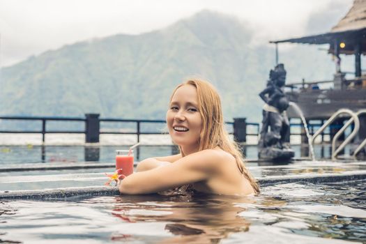 Geothermal spa. Woman relaxing in hot spring pool against the lake. hot springs concept. Drinking guava juice.