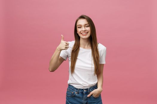 Happy young woman giving thumbs up on pink background