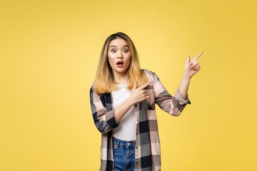 Smiling woman pointing finger side. Isolated portrait on yellow