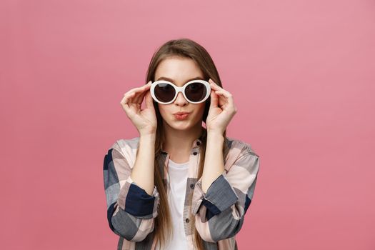 Photo closeup of charming womanwith long hairstyle wearing trendy sunglasses looking at camera with fashion look isolated over pink background.