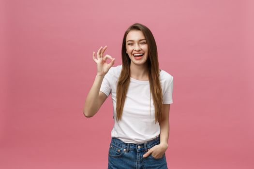 Attractive young adult woman showing ok sign. Expression emotion and feelings concept. Studio shot, isolated on pink background