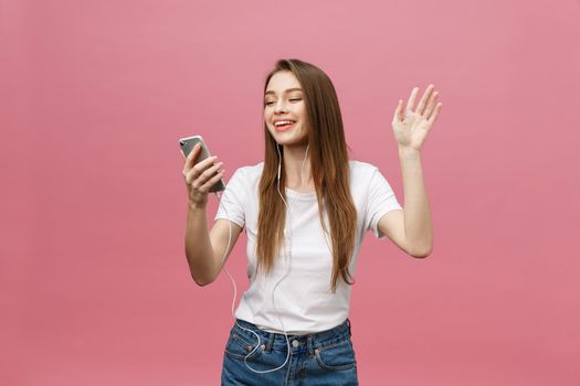 Lifestyle Concept. Young woman using phone for listening to music on pink background.