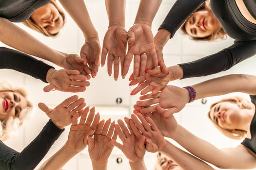 Team of people holding hands. Group of happy young women holding hands. Bottom view, low angle shot of human hands. Friendship and unity concept.