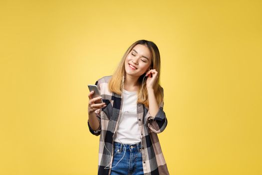 Fashion smiling asian woman listening to music in earphones over yellow background