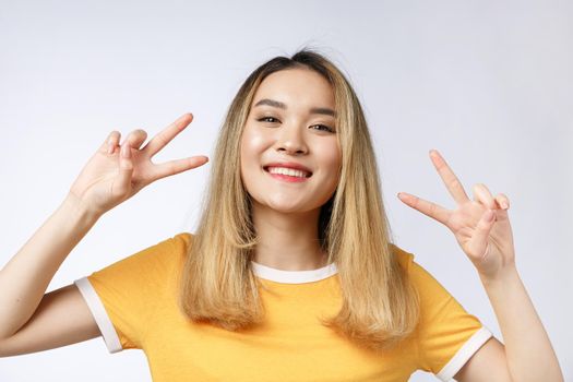 Happy young asian woman showing two fingers or victory gesture with blank copyspace area for text,Portrait of beautiful Asian woman isolated on white background.