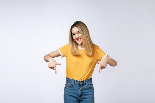 Beautiful young Asian woman point down to blank space on grey background