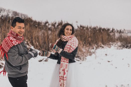 young man and woman running lying in the snow laughing fooling around having fun playing snowballs.bride and groom in love couple in knitted scarf and mittens in winter and snowflakes. mexican people