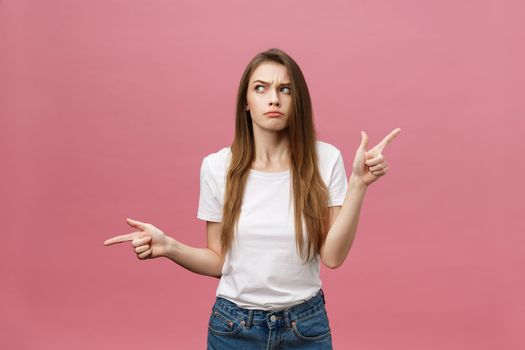 Closeup of serious strict young woman wears white shirt looks stressed and pointing up with finger isolated over pink background.