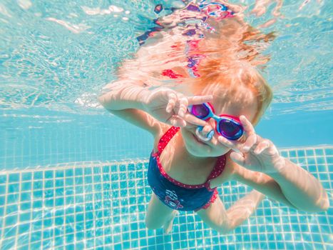 The little girl in the water park swimming underwater and smiling.