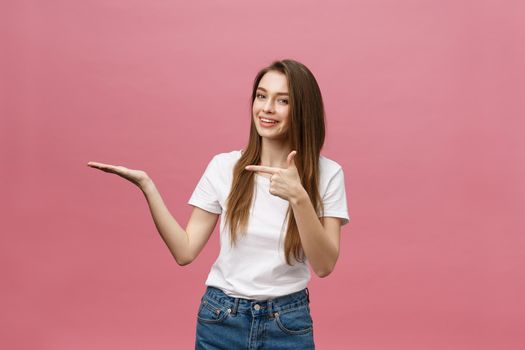 young girl with white shirt pointing hand on side to present a product on isolated pink background.