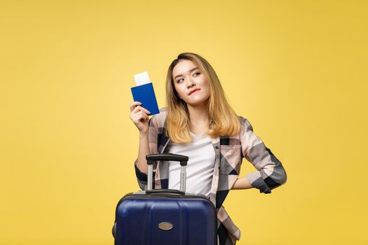 Woman travel. Young beautiful asian woman traveler holding passport ,suitcase and air ticket standing over yellow