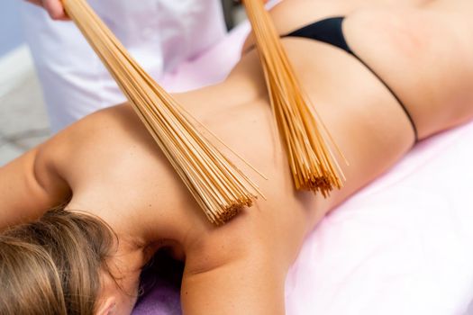 Woman masseuse doing double samurai massage with bamboo brooms in spa. Relaxing massage concept.