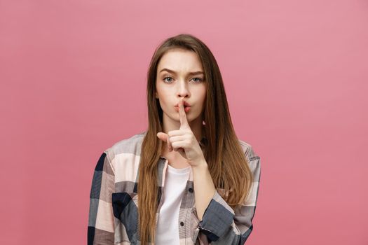 Portrait of young woman with finger on lips against pink wall.