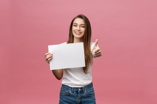 Young beauty woman hold blank card and showing thumbs up over pink background.