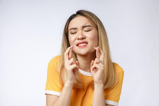 Portrait of praying young woman wearing casual clothing begging god please looking up with keeping fingers crossed isolated over gray background