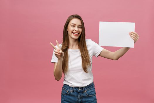 Close up portrait of positive laughing woman smiling and holding white big mockup poster isolated on pink background.