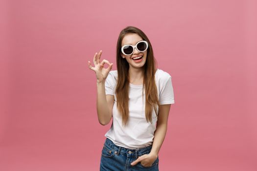 Attractive young adult woman showing ok sign. Expression emotion and feelings concept. Studio shot, isolated on pink background